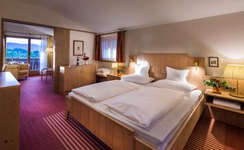 Zona notte della Suite Charme dell’Hotel St. Anton con letto matrimoniale, mobili in legno e illuminazione calda.
