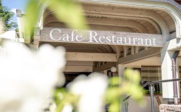 Entrance to the café restaurant of Hotel St. Anton with a wooden roof and blurred flowers in the foreground.