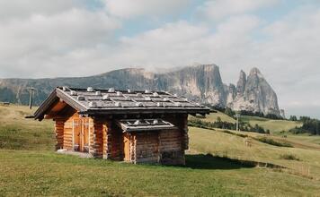 Holzhütte auf der Seiser Alm vor grünen Almwiesen und Dolomitenkulisse.