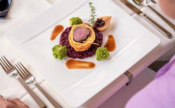 Angerichtete Hauptspeise mit Fleisch im Teigmantel, Rotkraut, Romanesco und Sauce auf einem weißen Teller.