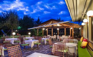 Terrace of Hotel St. Anton with set tables, metal chairs, and floor lamps in the evening.