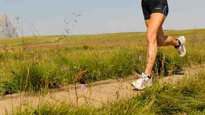 Female runner on the Seiser Alm with alpine meadows, a wooden hut and the Dolomites in the background.