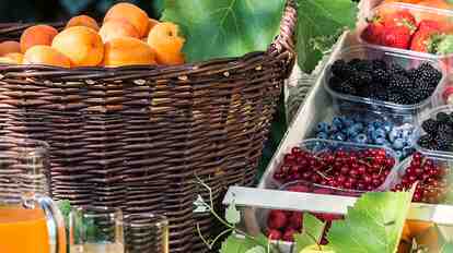 Basket with apricots, fresh berries, and fruit juices in the garden.