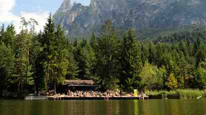 The Völser Weiher with a wooden hut and jetty; surrounded by forest and mountain scenery.