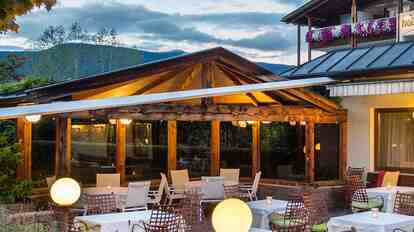 Evening-lit terrace of Hotel St. Anton with tables and chairs, surrounded by trees.