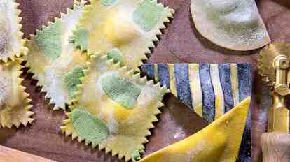 Freshly prepared ravioli with flour, a pastry wheel, and a rolling pin on a work surface.