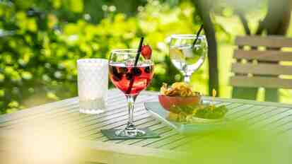 Primo piano di un tavolo in giardino con aperitivo per due e snack.