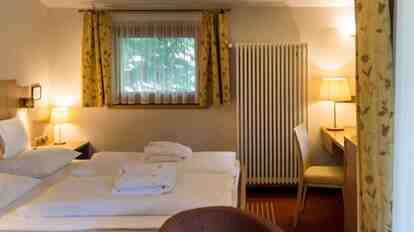 Charme St. Konstantin double room with wooden headboard, desk, and balcony overlooking greenery.