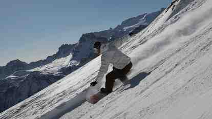 Snowboarder che scende lungo una pista davanti a montagne innevate.