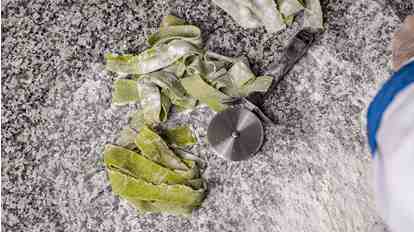 Fresh green pasta with flour and a pastry wheel on a stone work surface.