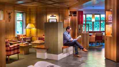 Foyer mit Holzvertäfelung, Sitzbereich und warmem Licht; ein Mann sitzt auf einer Bank und liest.