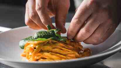 Fresh pasta with tomato sauce and green herbs is being plated on a white plate.