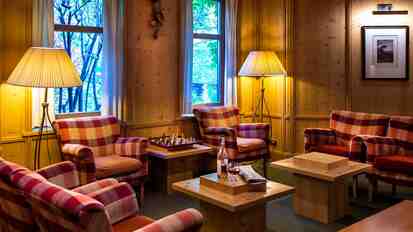 Gemütliche Lounge im alpinen Stil mit karierten Sesseln, Sofas, Holztischen und warm beleuchteten Holzwänden.