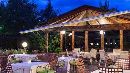 Abendlich beleuchtete Terrasse des Hotel St. Anton mit Tischen und Stühlen, umgeben von Bäumen.