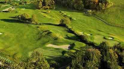 Golfplatz mit gepflegten Fairways und Sandbunkern, umgeben von Wald und grüner Landschaft.