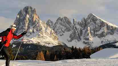 Two cross-country skiers in a winter landscape; in the background, a massive mountain backdrop.