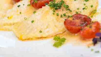 Plated appetizer with ravioli, tomatoes, herbs, and grated cheese.