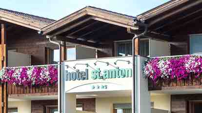 Nahaufnahme Hotel St. Anton mit Schriftzug und drei Sternen; Blumen auf den Balkonen.