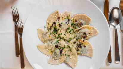 Schlutzkrapfen, ravioli altoatesini serviti su un piatto bianco con erbe aromatiche e formaggio.
