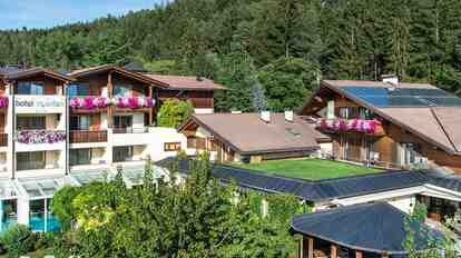 Hotel St. Anton mit blumengeschmückten Balkonen, Poolbereich und Garten vor dichtem Wald.