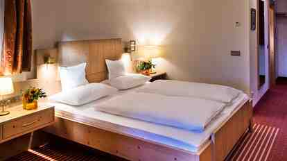Schlafbereich der Suite Charme St. Anton mit Doppelbett, Holzmöbeln, Nachttischlampen und Schreibtisch
