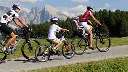 Famiglia durante un’escursione in bicicletta sull’Alpe di Siusi; sullo sfondo il paesaggio montano delle Dolomiti.