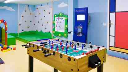 Sala giochi colorata dell’Hotel St. Anton con calcio balilla, parete da arrampicata, angolo giochi e vivaci pitture murali.